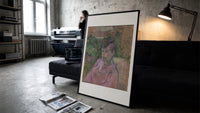 Woman in pink dress portrait print in a slim black frame leaning on a dark sofa in a concrete print studio
