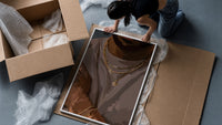 Layered Gold Chains on Taupe framed print being unpacked from protective bubble wrap and a box