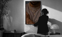 Layered Gold Chains on Taupe print in a slim black frame being hung on a sunlit wall in a monochrome room