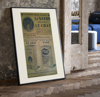 Vintage French soap advertisement with cat print in a black frame leaning beside a vintage door on parquet