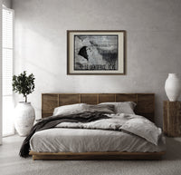 Woman's face with flowing hair reclining print in a dark wood frame above a rattan bed on a plaster wall