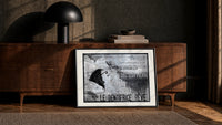 Woman's face with flowing hair reclining print in a black frame leaning against a walnut console in lamplight