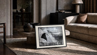 Woman's face with flowing hair reclining print in a slim black frame leaning on a travertine coffee table
