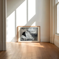 Woman's face with flowing hair reclining print in an oak frame on a sunlit wood floor beneath tall window light