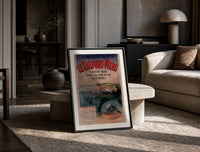 Coastal seaside town harbour view print in a black frame leaning on a travertine table in a sunlit lounge