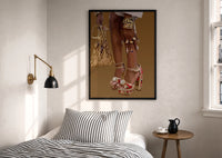 Legs in Jeweled Platform Heels print in a black frame above a bed with striped linens, a brass wall lamp and a sunlit window