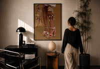 Legs in Jeweled Platform Heels print in a black frame on a sunlit plaster wall, a woman looking on beside a mushroom lamp