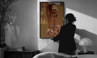 Legs in Jeweled Platform Heels print in a slim black frame being hung on a sunlit wall in a monochrome room