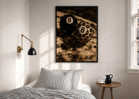 Leopard and Black 8 Balls print in a black frame above a bed with striped linens, a brass wall lamp and a sunlit window