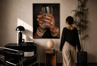 Leopard Nails and Gold Rings print in a black frame on a sunlit plaster wall, a woman looking on beside a mushroom lamp
