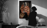 Leopard Nails and Gold Rings print in a slim black frame being hung on a sunlit wall in a monochrome room