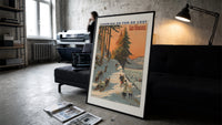 Winter sports scene with sledders and skiers print in a slim black frame leaning on a dark sofa in a concrete print studio