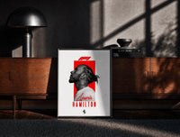 Black-framed Lewis Hamilton profile portrait print on a moody console with designer coffee-table books