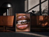 Black-framed Lips Holding a Daddy Chain print on the floor in front of a dark wooden console