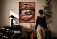 Lips Holding a Daddy Chain print in a black frame on a sunlit plaster wall, a woman looking on beside a mushroom lamp