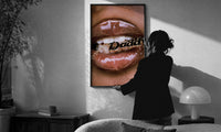 Lips Holding a Daddy Chain print in a slim black frame being hung on a sunlit wall in a monochrome room