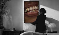 Lips with Decorative Gold Grillz print in a slim black frame being hung on a sunlit wall in a monochrome room