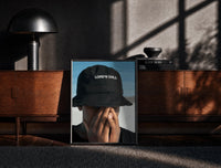 Black-framed Lord's Child Bucket Hat print on the floor in front of a dark wooden console