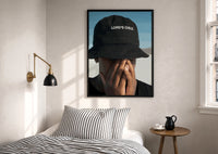 Lord's Child Bucket Hat print in a black frame above a bed with striped linens, a brass wall lamp and a sunlit window