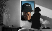 Lord's Child Bucket Hat print in a slim black frame being hung on a sunlit wall in a monochrome room