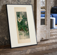 White hellebore flowers with sparrows print in a black frame leaning beside a vintage door on parquet