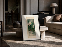 White hellebore flowers with sparrows print in a black frame leaning on a travertine table in a sunlit lounge