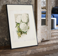 White chrysanthemum flowers with leaves print in a black frame leaning beside a vintage door on parquet