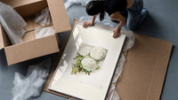 White chrysanthemum flowers with leaves framed print being unpacked from protective bubble wrap and a box