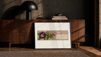 Purple pansy and pink blossom bouquet print in a black frame leaning against a walnut console in lamplight