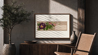 Purple pansy and pink blossom bouquet print in a wood frame above a fluted sideboard beside an olive tree