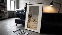 Robin perched on bare branch print in a slim black frame leaning on a dark sofa in a concrete print studio