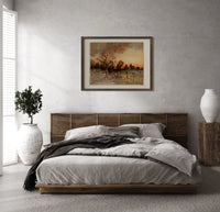 Winter landscape with ice skaters at dusk print in a dark wood frame above a rattan bed on a plaster wall