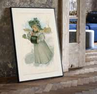 Blonde girl in plumed hat holding violets print in a black frame leaning beside a vintage door on parquet
