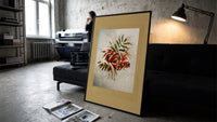 Autumn-tinted leaves branch print in a slim black frame leaning on a dark sofa in a concrete print studio