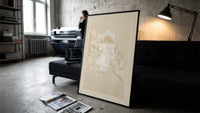 Child in white winter coat and bonnet print in a slim black frame leaning on a dark sofa in a concrete print studio