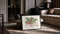 Holly sprig with red berries print in a slim black frame leaning on a travertine coffee table