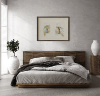 Two young girls holding flowers print in a dark wood frame above a rattan bed on a plaster wall