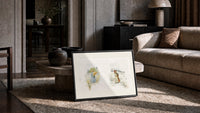Two young girls holding flowers print in a slim black frame leaning on a travertine coffee table