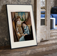 Two Victorian women looking at painting print in a black frame leaning beside a vintage door on parquet