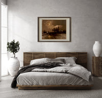 Moonlit winter church landscape print in a dark wood frame above a rattan bed on a plaster wall