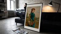 Victorian woman holding flower basket print in a slim black frame leaning on a dark sofa in a concrete print studio