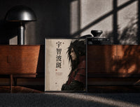 Black-framed Anime warrior in red armor print on a moody console with designer coffee-table books