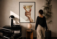 Martini Glass print in a black frame on a sunlit plaster wall, a woman looking on beside a mushroom lamp