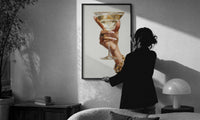 Martini Glass print in a slim black frame being hung on a sunlit wall in a monochrome room