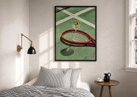 Racket and Martini print in a black frame above a bed with striped linens, a brass wall lamp and a sunlit window