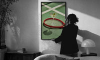 Racket and Martini print in a slim black frame being hung on a sunlit wall in a monochrome room