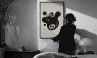 Melting 8 Ball print in a slim black frame being hung on a sunlit wall in a monochrome room