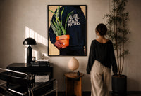 Mental Health Matters Hoodie and Potted Plant print in a black frame on a sunlit plaster wall, a woman looking on beside a mushroom lamp