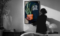 Mental Health Matters Potted Plant print in a slim black frame being hung on a sunlit wall in a monochrome room