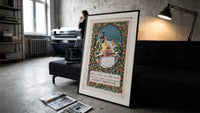 Snow-covered cottage in winter print in a slim black frame leaning on a dark sofa in a concrete print studio
